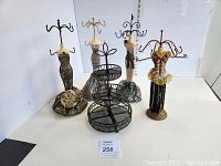 Front view of four fabric dress form jewelry holders and one three-tier metal mesh jewelry stand on white background