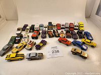 Wide view of 37 Hot Wheels toy cars arranged in rows showing different models and colors including muscle cars, trucks, and specialty vehicles.
