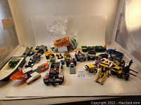 Full view of varied partial Lego vehicles and loose components arranged on white surface, showing assortment of car and construction vehicle parts in different colors.