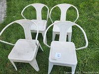 Four white metal outdoor chairs placed on grass showing wear from outdoor exposure.
