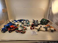 Grouped loose LEGO vehicle parts on white backdrop, showing police vehicles, garbage truck, airplane, sports car, pickup truck, and construction vehicles.