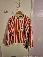 Front view of jacket showing red and white vertical stripes with a Mickey Mouse face on the front pocket and ribbed cuffs and hem.
