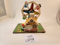 Side angle of vintage Fisher Price Little People Ferris Wheel toy showing colorful spinning wheel, figures seated, and base with ticket booth graphic.