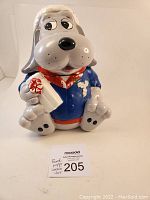Front view of the vintage Pound Puppy cookie jar showing the dog's face, blue jacket, red scarf, and the white bone with red paw print it is holding.