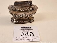 Front angle view of silver-toned vintage Ronson "Georgian" table lighter showing ornate decorative design and lighter mechanism on top.