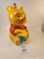 Front view of ceramic Winnie the Pooh cookie jar holding honey pot with bee on head.