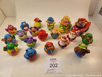 Photo showing full set of 22 Weebles arranged on white background. Characters include animals, a red fire hydrant, a rocking horse rider, and a red car with driver.
