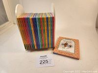 Photo of 19 Winnie the Pooh books lined up in white wooden shelf stand with one book placed beside it showing the cover titled 'Pooh and Piglet Go Hunting'.