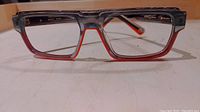 Front view of rectangular designer eyewear glasses showing gradient gray to red frames with orange details inside.