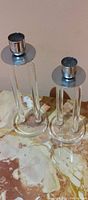 Pair of clear lucite MCM candle holders with silver metal tops of different heights on a marble surface.