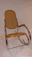 Front view of MCM rocking chair showing chrome tubular frame, cane seat, backrest and armrests
