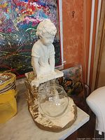 Side view of sculpture showing boy kneeling and clear glass bowl placed on base