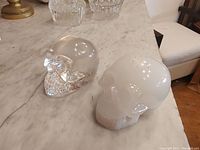 Pair of resin skulls on marble surface, clear and white colors shown from top angle