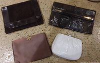 Photo showing 4 vintage ladies handbags arranged on floor: black patent leather flap handbag, dark brown faux snakeskin clutch, mauve fabric handbag with floral button, white glossy patent leather coin purse.