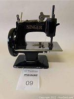 Front and side view of black Singer child's sewing machine showing gold logo and overall machine body with minor paint wear.