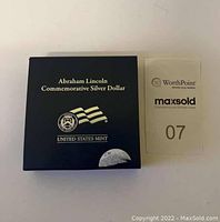 United States Mint Abraham Lincoln Commemorative Silver Dollar box and certificate of authenticity card side-by-side on a white background