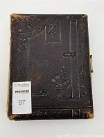 Front cover of the antique cabinet photo album showing embossed floral and geometric pattern on black leather with wear on edges and corners