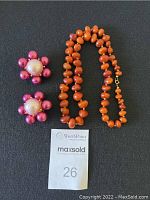 Pair of Ben Amun pink and white flower-shaped clip-on earrings with Baltic amber bead necklace on black background