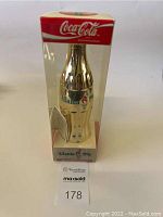 Front view of the sealed limited edition gold Coca Cola bottle with 1996 Atlanta Olympics logo inside original packaging, showing bottle and branding.