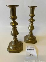 Front view of two heavy brass candlestick holders with hexagonal bases and tiered stepped designs showing overall shape and size.