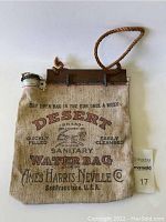 Full front view of vintage canvas water bag canteen showing printed branding and metal cap with rope handle.