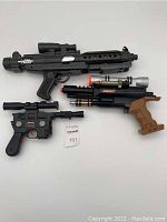 Three vintage Star Wars blasters laid flat, showing sizes, colors, and overall condition.