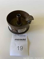 Front view showing central cigarette tube, curved cigarette rest with embossed text, and Quartermaster Corps insignia on the side.