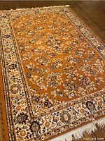 Full view of rectangular gold-toned rug with floral pattern on wood floor