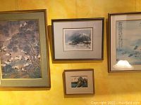Four framed Asian artworks displayed on a yellow wall: large crane painting, two misty landscapes, one with calligraphy, and a small wave painting.