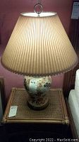 First lamp shown full height with pleated lampshade and floral ceramic base on rattan table