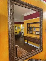 Full view of large decorative wall mirror hung on yellow wall, reflecting room interior