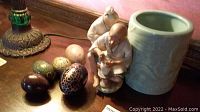 Six decorative eggs of various colors and designs, small figurine, and green glazed pot arranged on a wooden surface.