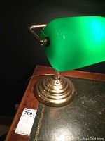 Side view of desk lamp showing green glass shade, brass arm and base, and pull chain switch.