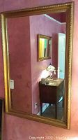 Full view of the rectangular mirror mounted on a pink wall, showcasing its gold ornate frame and reflection of room details.