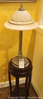 Full view of the lamp with glass shade sitting on the wooden stand by a yellow wall.