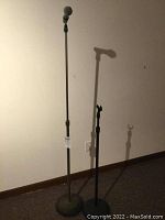 Photo of two black adjustable microphone stands, one with a microphone attached at the top with a spherical mesh grille.