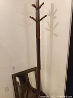 Wooden coat stand with several coat hooks and four legs, photographed leaning against a wall.
