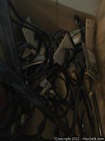 Box filled with nine black metal plant brackets with curved hooks and scroll designs.