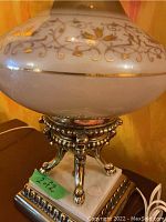 Photo showing the base of one lamp with metal claw feet and ornate silver detailing, glass shade with gold floral pattern visible above
