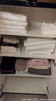 Photo of white, beige, pink, gray, and dark colored towels folded and stacked on three shelves in a linen cupboard.