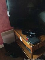 LG 42 inch TV on wooden stand with remotes and cables visible on stand.