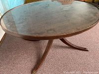 Full oval coffee table showing glass top and curved wooden legs on carpet.