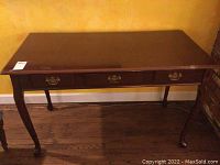 Full front view showing the polished surface, three drawers with ornate pulls, and cabriole legs with carved feet.