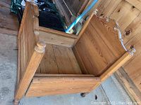 Photo of antique wooden toddler bed at an angle showing carved posts and headboard, and adjustable frame.