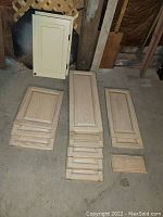 Photo of a collection of cream-colored wooden cabinet doors in various sizes stacked on floor next to a large dark wood beam.