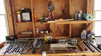 Full view of the workbench shelf with chain saw sharpener mounted, various oils and lubricants, tools, and hardware items spread on shelf.