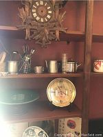 Clock mounted on shelf with various metal cups and a decorative plate and Japanese prints nearby