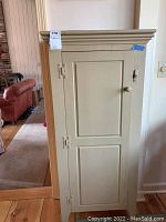 Front view of closed cupboard showing door with two recessed panels and decorative molding at top.