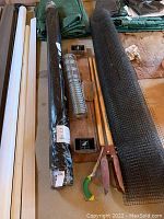 Overview of deer fencing rolls, wire mesh, wooden stakes, and garden tools arranged on floor.