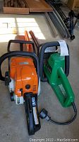 Both hedge trimmer and chainsaw side by side on concrete floor